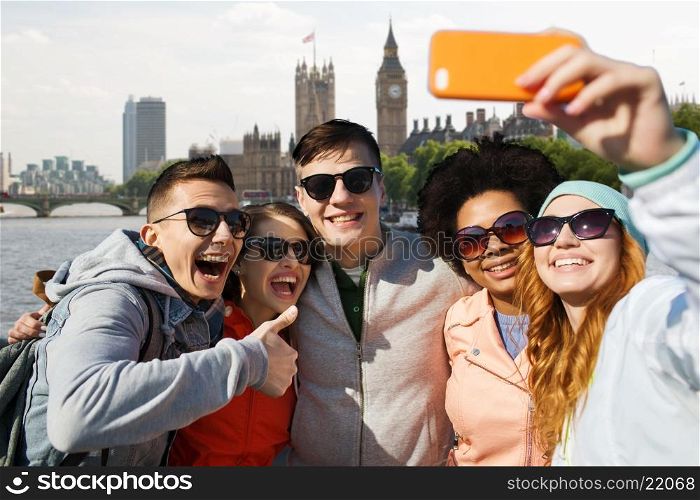 tourism, travel, people, leisure and technology concept - group of smiling teenage friends taking selfie with smartphone over houses of parliament and thames river in london background