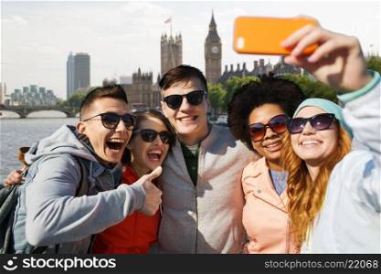 tourism, travel, people, leisure and technology concept - group of smiling teenage friends taking selfie with smartphone over houses of parliament and thames river in london background