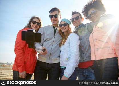 tourism, travel, people, leisure and technology concept - group of smiling teenage friends taking selfie with smartphone and monopod on city street