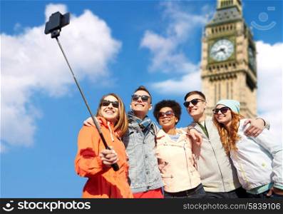 tourism, travel, people, leisure and technology concept - group of smiling teenage friends taking selfie with smartphone and monopod over london big ben tower background
