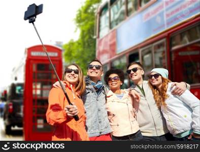 tourism, travel, people, leisure and technology concept - group of smiling teenage friends taking selfie with smartphone and monopod over london city street background