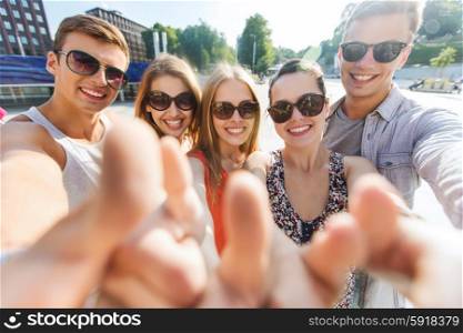 tourism, travel, people, leisure and technology concept - group of smiling teenage friends taking selfie and showing thumbs up outdoors