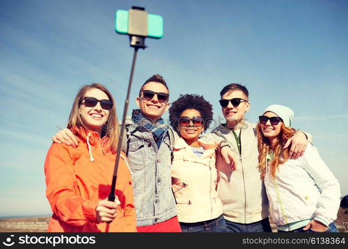 tourism, travel, people, leisure and technology concept - group of smiling teenage friends taking selfie with smartphone and monopod on city street