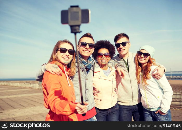 tourism, travel, people, leisure and technology concept - group of smiling teenage friends taking selfie with smartphone and monopod on city street