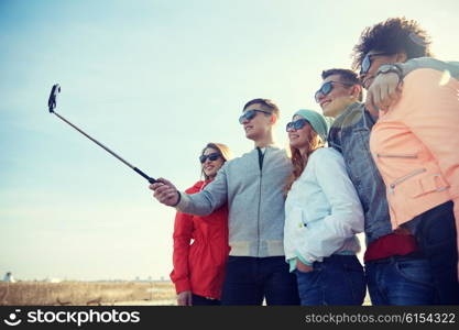 tourism, travel, people, leisure and technology concept - group of smiling teenage friends taking selfie with smartphone and monopod on city street