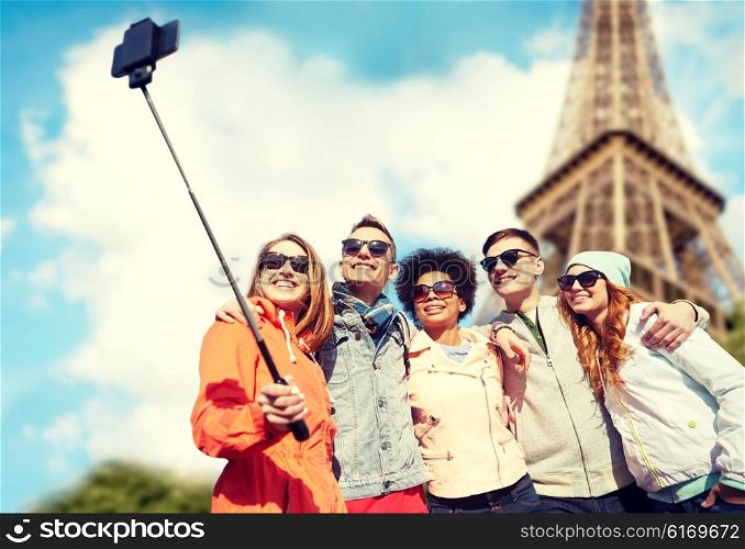 tourism, travel, people, leisure and technology concept - group of smiling teenage friends taking selfie with smartphone and monopod over paris eiffel tower background