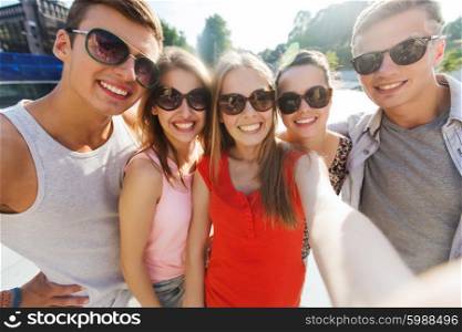tourism, travel, people, leisure and technology concept - group of smiling teenage friends taking selfie outdoors