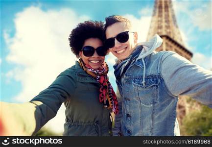 tourism, travel, people, leisure and technology concept - happy international teenage couple taking selfie over paris eiffel tower background