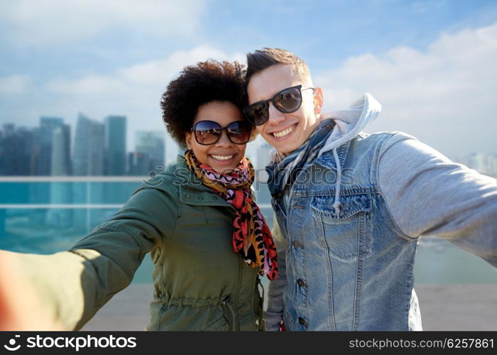 tourism, travel, people, leisure and technology concept - happy international teenage couple taking selfie over singapore city background