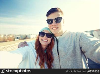 tourism, travel, people, leisure and technology concept - happy teenage couple taking selfie on city street
