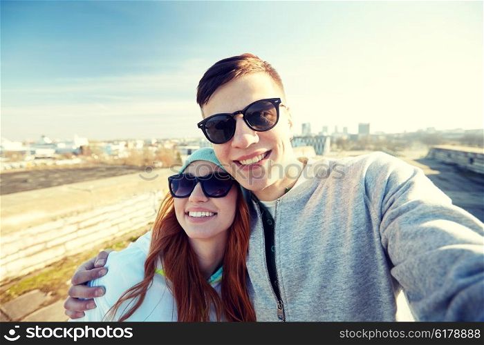 tourism, travel, people, leisure and technology concept - happy teenage couple taking selfie on city street