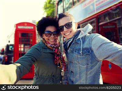 tourism, travel, people, leisure and technology concept - happy teenage international couple taking selfie over london city street background