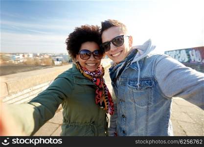 tourism, travel, people, leisure and technology concept - happy teenage international couple taking selfie on city street