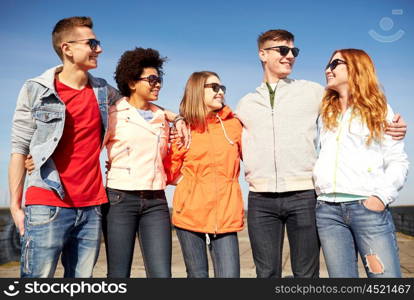 tourism, travel, people, leisure and teenage concept - group of happy friends in sunglasses hugging and talking on city street