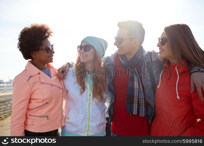 tourism, travel, people, leisure and teenage concept - group of happy friends in sunglasses hugging and talking on city street