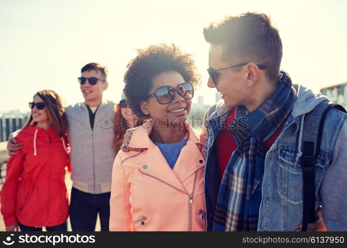 tourism, travel, people, leisure and teenage concept - group of happy friends in sunglasses hugging and talking on city street