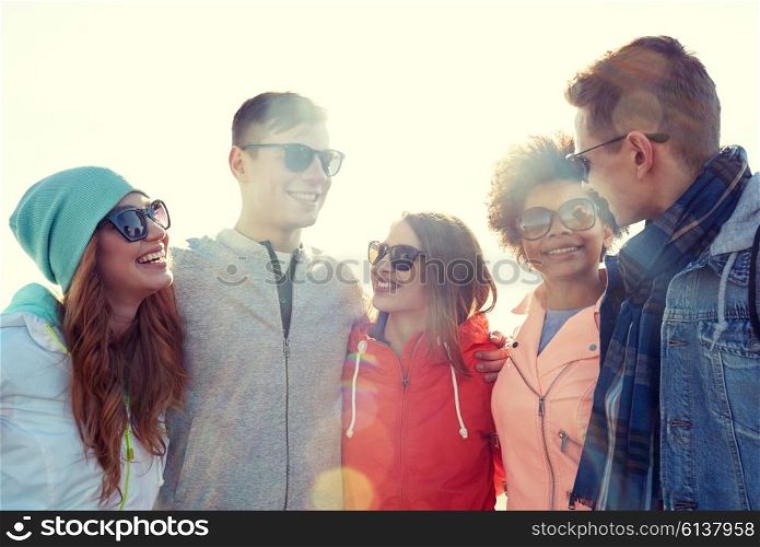 tourism, travel, people, leisure and teenage concept - group of happy friends in sunglasses hugging and talking on city street