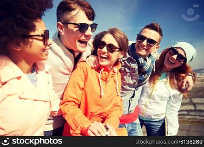tourism, travel, people, leisure and teenage concept - group of happy friends in sunglasses hugging and laughing on city street