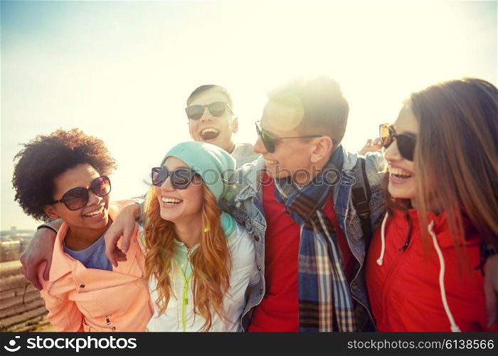 tourism, travel, people, leisure and teenage concept - group of happy friends in sunglasses hugging and laughing on city street