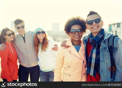tourism, travel, people, leisure and teenage concept - group of happy friends in sunglasses hugging on city street