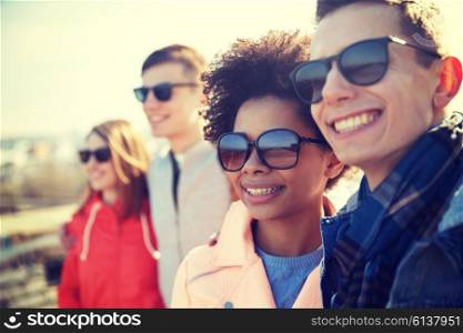 tourism, travel, people, leisure and teenage concept - group of smiling teenagers in sunglasses hugging on city street