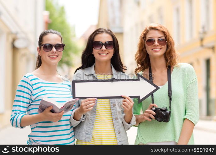 tourism, travel, vacation, direction and friendship concept - smiling teenage girls with white arrow showing direction outdoors