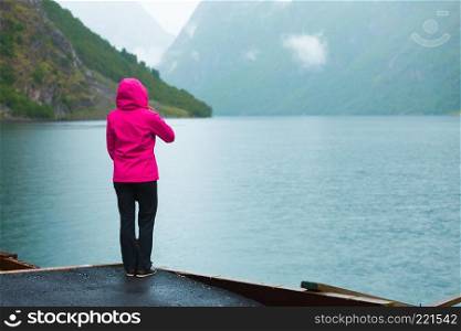 Tourism vacation and travel. Female tourist looking at mountains and fjord Sognefjord in Norway, Scandinavia. Misty foggy day, rainy weather. Tourist looking at mountains and fjord Norway, Scandinavia.