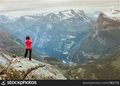 Tourism vacation and travel. Female tourist taking photo with camera, enjoying Geiranger fjord and mountains landscape from Dalsnibba Plateau viewpoint, Norway Scandinavia.. Tourist taking photo from Dalsnibba viewpoint Norway