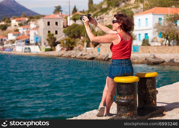 Tourism vacation and travel. Mature woman tourist in greek resort marina taking photo with camera. Sea blue background. Tourist take photo in greek marina