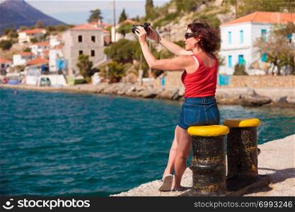 Tourism vacation and travel. Mature woman tourist in greek resort marina taking photo with camera. Sea blue background. Tourist take photo in greek marina
