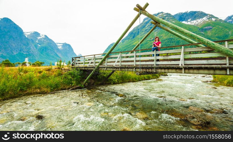 Tourism vacation and travel. Woman tourist relaxing on bridge, looking at mountains landscape in norwegian village Oppstryn, Sogn og Fjordane county. Norway Scandinavia.. Tourist relaxing on bridge in village Oppstryn Norway