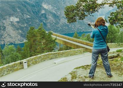Tourism vacation and travel. Woman tourist taking photo with camera, enjoying Aurland fjord view from Stegastein viewpoint, Norway Scandinavia.. Tourist taking photo from Stegastein viewpoint Norway