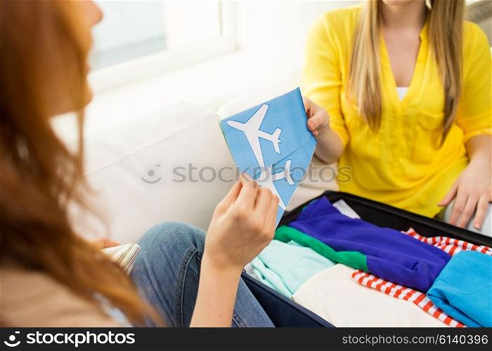 tourism, vacation, luggage and people concept - close up of women with airplane tickets and clothes in travel bag at home