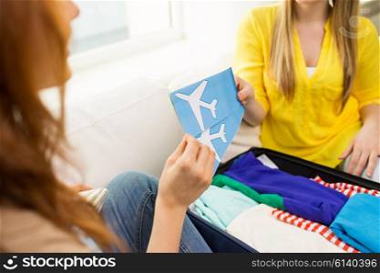tourism, vacation, luggage and people concept - close up of women with airplane tickets and clothes in travel bag at home