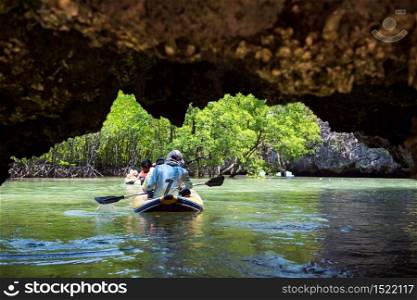 Tourist and sailor canoeing through Tham Lod (small grotto cave) of Karst formations to visit lagoon and mangrove tree jungle swamp in Phang Nga bay, Thailand. Famous travel destinaton in summer.