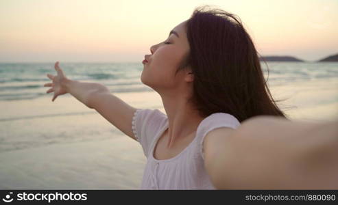 Tourist Asian woman selfie on beach, young beautiful female happy smiling using mobile phone taking selfie on beach near sea when sunset in evening. Lifestyle women travel on beach concept.