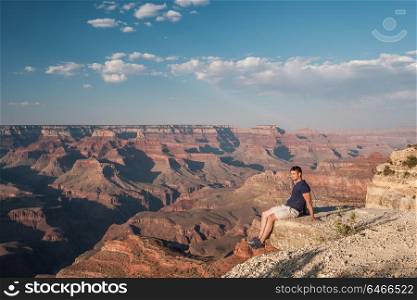 Tourist at Grand Canyon sitting on the rock edge, Arizona, USA
