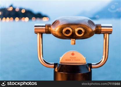 Tourist binoculars on the lake Lago di Garda, evening scene with water and mountains