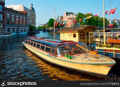 Tourist boats moored in Amsterdam canal pier on sunset. Amsterdam, Netherlands. Tourist boats moored in Amsterdam canal pier on sunset