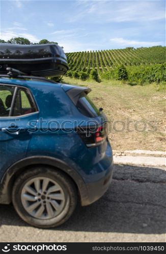 Tourist car in vineyards. Countryside and car with luggage box on top. Rural tourism concept with car and wine grapes on background. Travel concept.