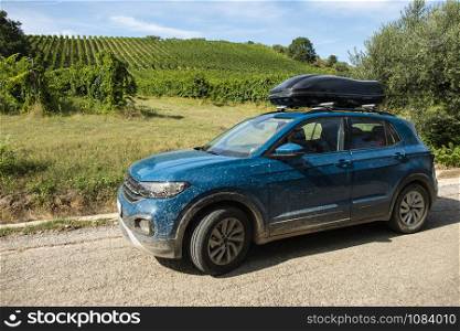 Tourist car in vineyards. Countryside and car with luggage box on top. Rural tourism concept with car and wine grapes on background. Travel concept.