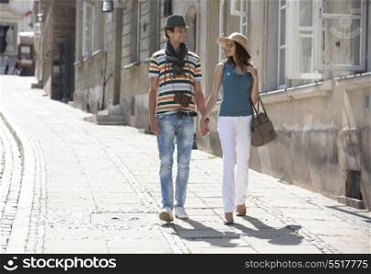 Tourist couple holding hands while walking on sidewalk