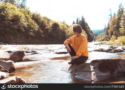 tourist girl sitting on the bank of a mountain river