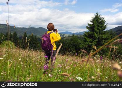 tourist girl with a backpack and camera standing in the meadow at the mountains. Carpathians. Ukraine