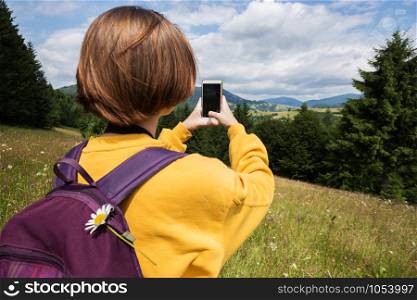 tourist girl with a backpack and smartphone standing in the meadow at the mountains. Carpathians. Ukraine