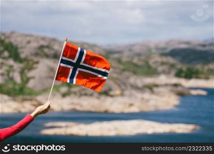 Tourist hand holding norwegian flag on rocky stone sea coast background.. Tourist with norwegian flag on sea coast