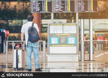 Tourist man looking at flight information board in international airport terminal