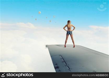 Tourist on airplane wing. Traveler woman in bikini and shorts on airplane wing
