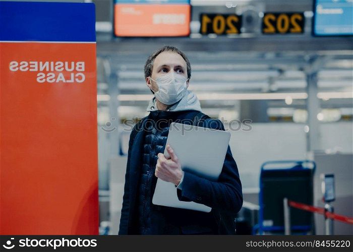Tourist poses in airport, wants to return home during quarantine and world pandemia, wears protective medical mask against coronavirus, avoids infection and virus spreading. Traveling during outbreak