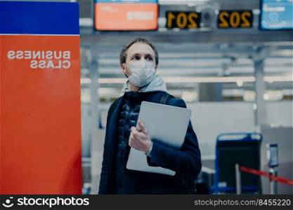 Tourist poses in airport, wants to return home during quarantine and world pandemia, wears protective medical mask against coronavirus, avoids infection and virus spreading. Traveling during outbreak